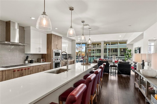 kitchen with pendant lighting, wall chimney range hood, decorative backsplash, stainless steel double oven, and white cabinetry