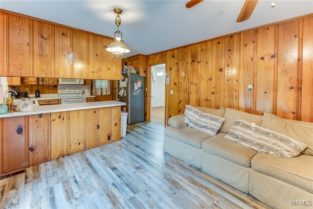 kitchen featuring kitchen peninsula, light wood-type flooring, white appliances, hanging light fixtures, and wood walls