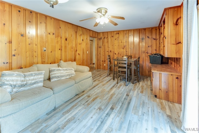 living room featuring ceiling fan, wood walls, and light wood-type flooring