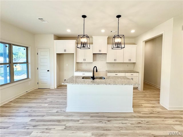 kitchen with visible vents, an island with sink, a sink, backsplash, and white cabinets