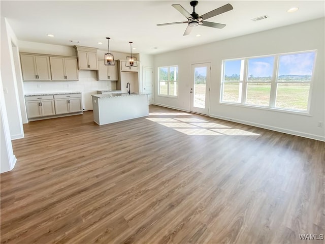 kitchen with light stone counters, an island with sink, wood-type flooring, and decorative light fixtures