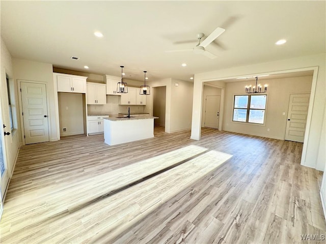 kitchen with a kitchen island with sink, a sink, decorative backsplash, white cabinets, and open floor plan