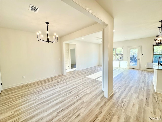 empty room with light wood finished floors, a notable chandelier, baseboards, and visible vents