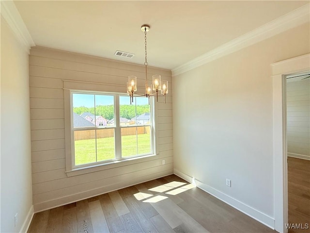 unfurnished dining area featuring wood finished floors, visible vents, ornamental molding, baseboards, and a notable chandelier