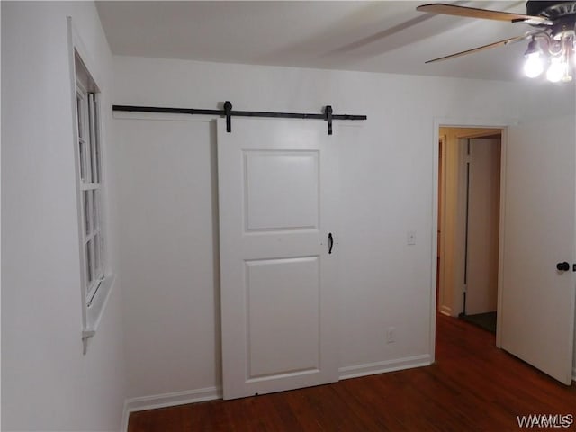 unfurnished bedroom featuring dark hardwood / wood-style flooring, a barn door, and ceiling fan