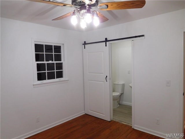 unfurnished bedroom featuring ceiling fan, a barn door, dark hardwood / wood-style floors, and connected bathroom