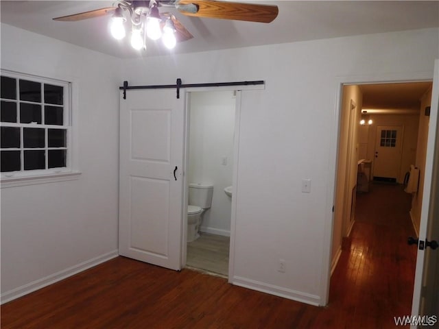 unfurnished bedroom featuring dark hardwood / wood-style floors, a barn door, ceiling fan, and ensuite bath