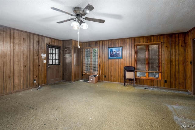 interior space with a textured ceiling, ceiling fan, and wood walls