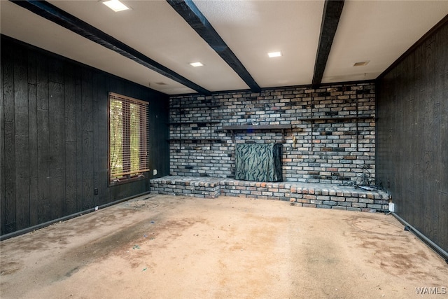 unfurnished living room featuring beamed ceiling, wooden walls, and a brick fireplace