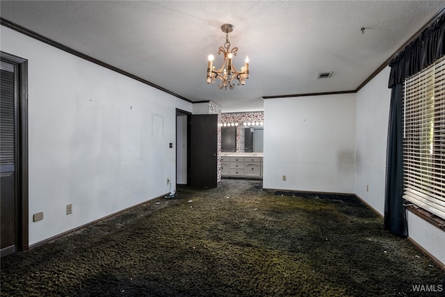 empty room with ornamental molding, dark carpet, a textured ceiling, and an inviting chandelier