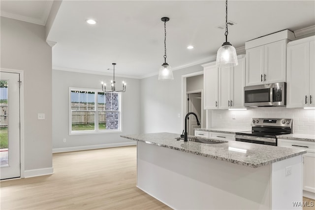 kitchen with stainless steel appliances, sink, white cabinets, hanging light fixtures, and an island with sink