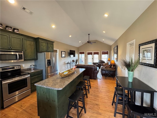 kitchen with a kitchen bar, appliances with stainless steel finishes, vaulted ceiling, and light wood-type flooring