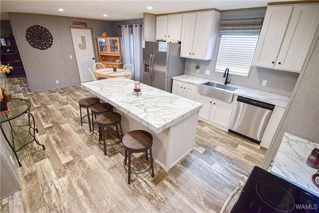 14371 Paul Mills Rd, Buhl, AL 35446 - kitchen with stainless steel appliances, light wood finished floors, a kitchen bar, white cabinetry, and a center island with sink
