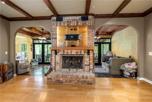 living area featuring arched walkways, plenty of natural light, ceiling fan with notable chandelier, and beam ceiling