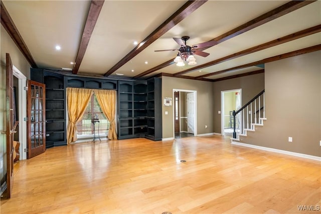 unfurnished living room with ceiling fan, stairway, baseboards, beamed ceiling, and light wood-style floors