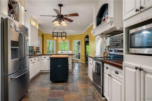 kitchen with ceiling fan, appliances with stainless steel finishes, stone tile flooring, wood counters, and ornamental molding