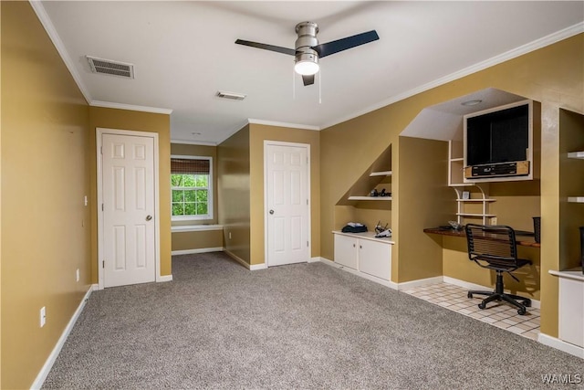unfurnished office with built in desk, carpet, a ceiling fan, visible vents, and ornamental molding