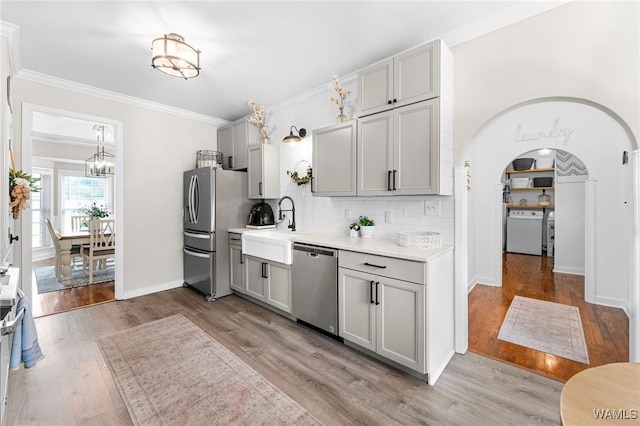 kitchen featuring stainless steel appliances, arched walkways, a sink, gray cabinetry, and ornamental molding