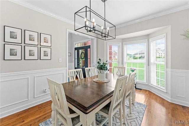 dining area with a chandelier, wood finished floors, wainscoting, plenty of natural light, and ornamental molding