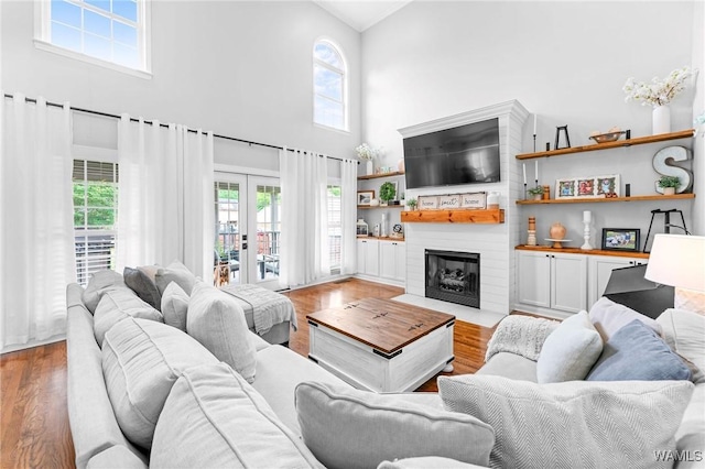 living room featuring a high ceiling, wood finished floors, healthy amount of natural light, and a fireplace with flush hearth