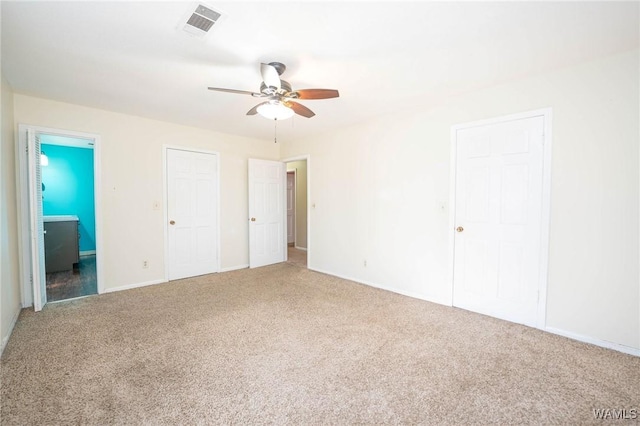 unfurnished bedroom featuring carpet floors, ceiling fan, multiple closets, and connected bathroom