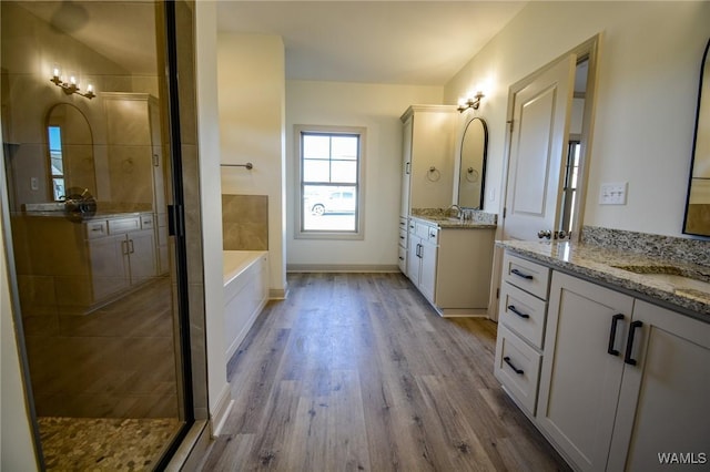 bathroom featuring baseboards, wood finished floors, a garden tub, a shower stall, and a sink