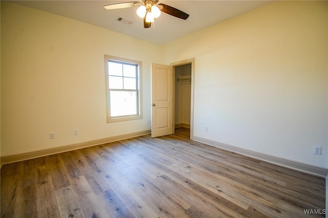 unfurnished bedroom featuring baseboards, visible vents, a ceiling fan, wood finished floors, and a walk in closet