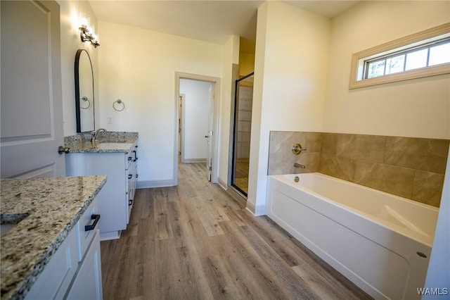 bathroom with wood finished floors, two vanities, baseboards, a bath, and a stall shower