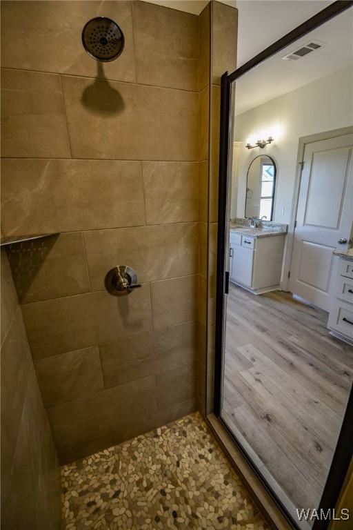 full bathroom featuring vanity, wood finished floors, a tile shower, and visible vents