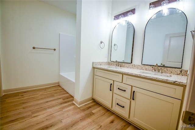 bathroom with double vanity, baseboards, a sink, and wood finished floors