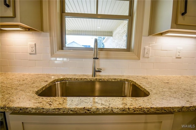 interior details featuring a sink, backsplash, and light stone countertops