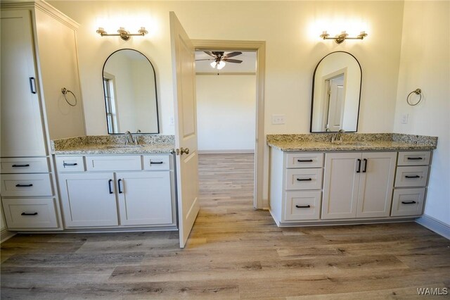 full bathroom with baseboards, two vanities, a sink, and wood finished floors