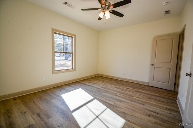 unfurnished room featuring wood finished floors, visible vents, and baseboards