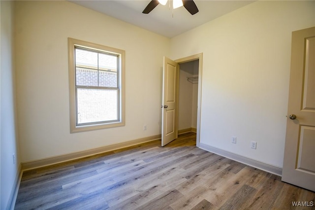 unfurnished bedroom with ceiling fan, a walk in closet, light wood-style flooring, and baseboards