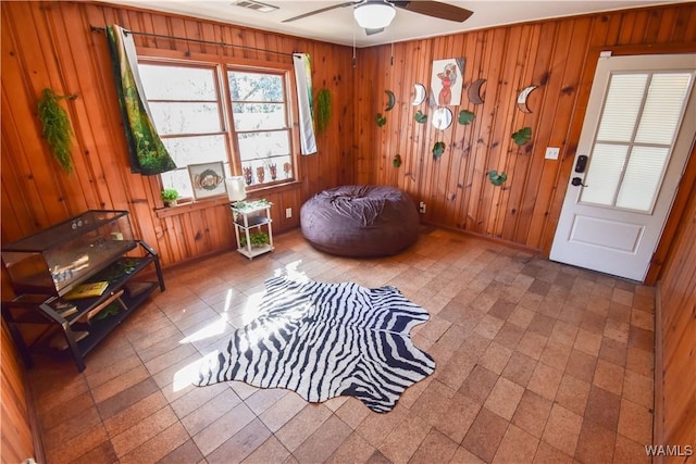 interior space with visible vents, a ceiling fan, and wooden walls