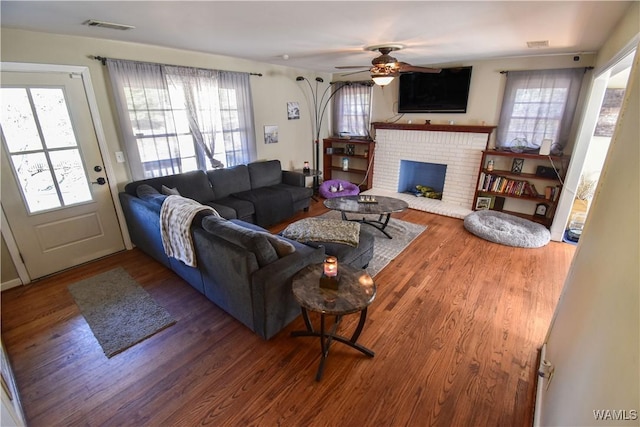 living room featuring ceiling fan, a brick fireplace, wood finished floors, and visible vents