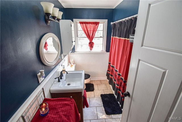 full bath with a shower with curtain, tile patterned flooring, wainscoting, and a sink