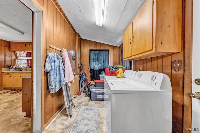 washroom with washer and dryer, wood walls, and cabinets