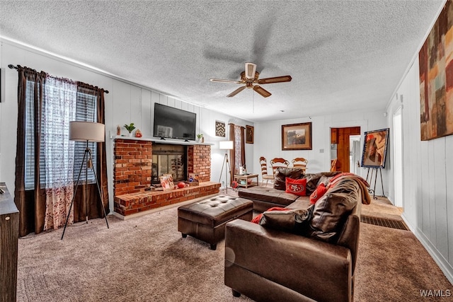 living room with ceiling fan, a fireplace, carpet floors, and a textured ceiling