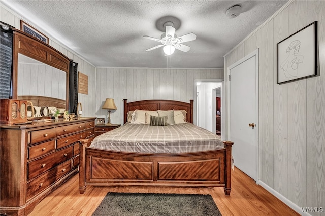 bedroom featuring ceiling fan, light hardwood / wood-style flooring, a textured ceiling, and wooden walls