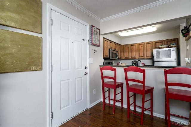 kitchen featuring brown cabinets, dark countertops, stainless steel microwave, ornamental molding, and fridge