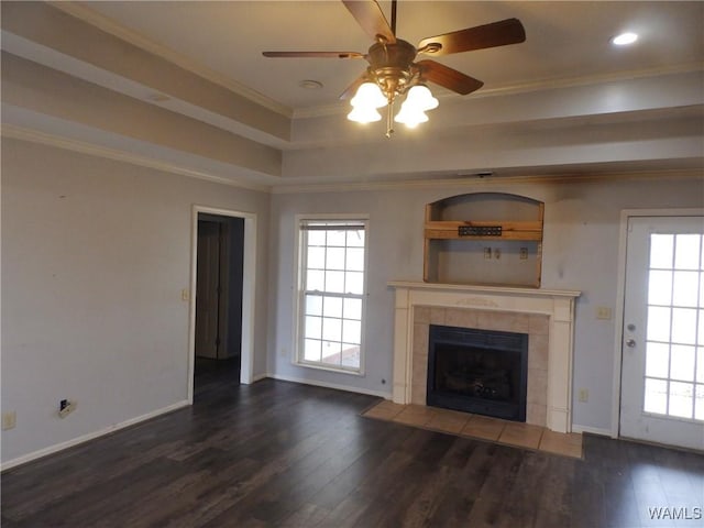 unfurnished living room with dark wood-type flooring, a tray ceiling, a fireplace, and crown molding