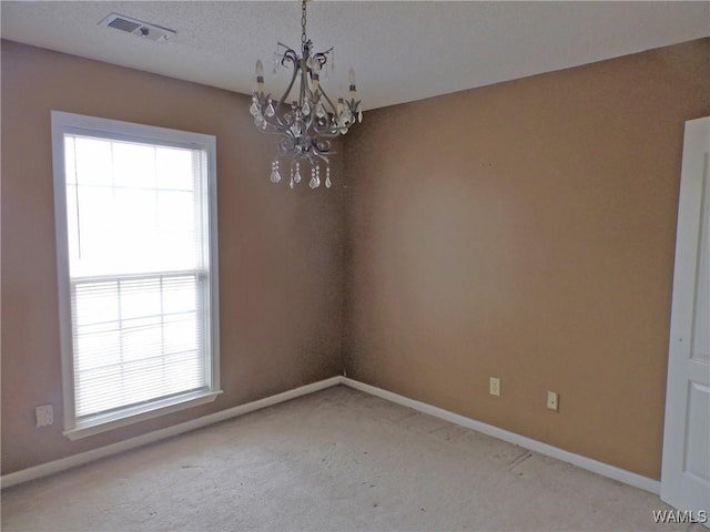 carpeted spare room featuring visible vents, baseboards, and an inviting chandelier