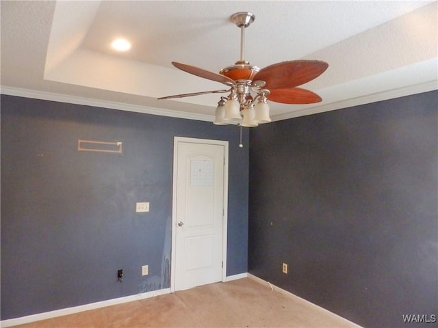 carpeted empty room featuring ornamental molding, a tray ceiling, ceiling fan, and baseboards