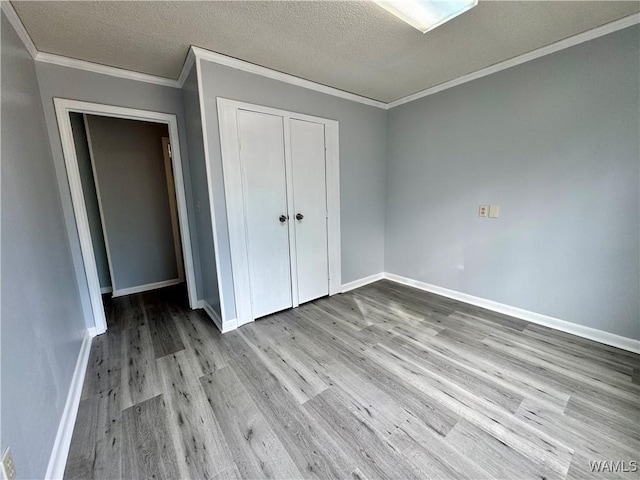 unfurnished bedroom featuring light hardwood / wood-style flooring, crown molding, a textured ceiling, and a closet