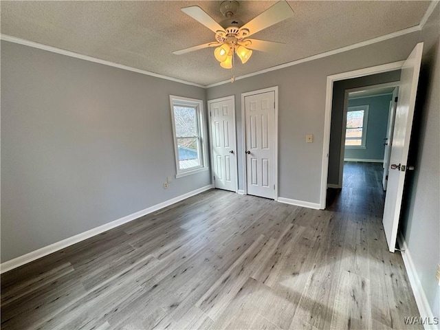 unfurnished bedroom with multiple closets, ceiling fan, light hardwood / wood-style floors, a textured ceiling, and ornamental molding