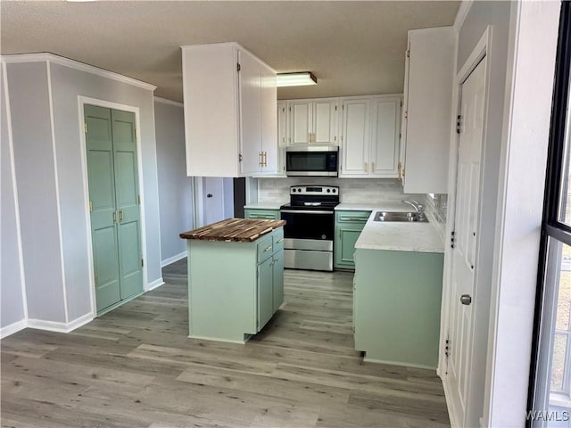 kitchen with appliances with stainless steel finishes, sink, white cabinets, butcher block countertops, and a kitchen island