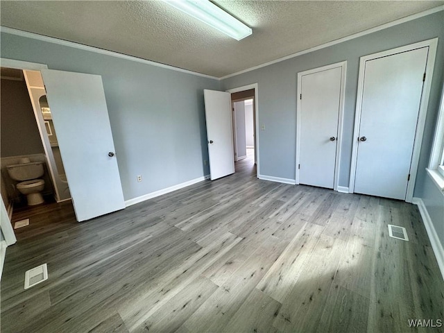 unfurnished bedroom with two closets, light wood-type flooring, a textured ceiling, connected bathroom, and ornamental molding