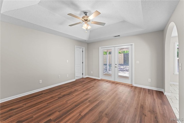 spare room featuring dark wood-style flooring, french doors, a tray ceiling, ceiling fan, and arched walkways