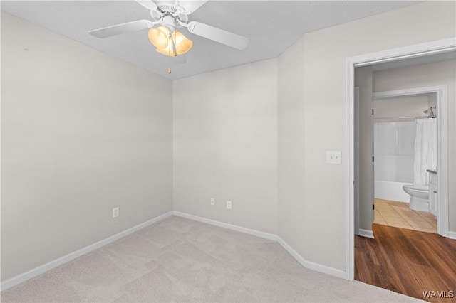 unfurnished bedroom featuring carpet flooring, ensuite bath, baseboards, and a ceiling fan